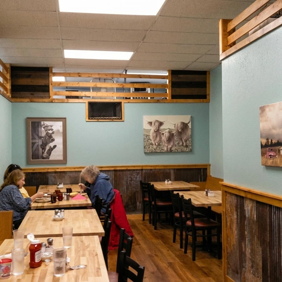 Cozy restaurant dining room with wooden tables, two diners, rustic barn artwork, and teal walls.